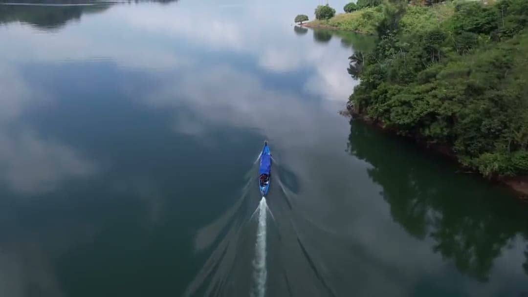 Vista aérea de un embalse de aguas tranquilas rodeado de selva, con una canoa a lo lejos